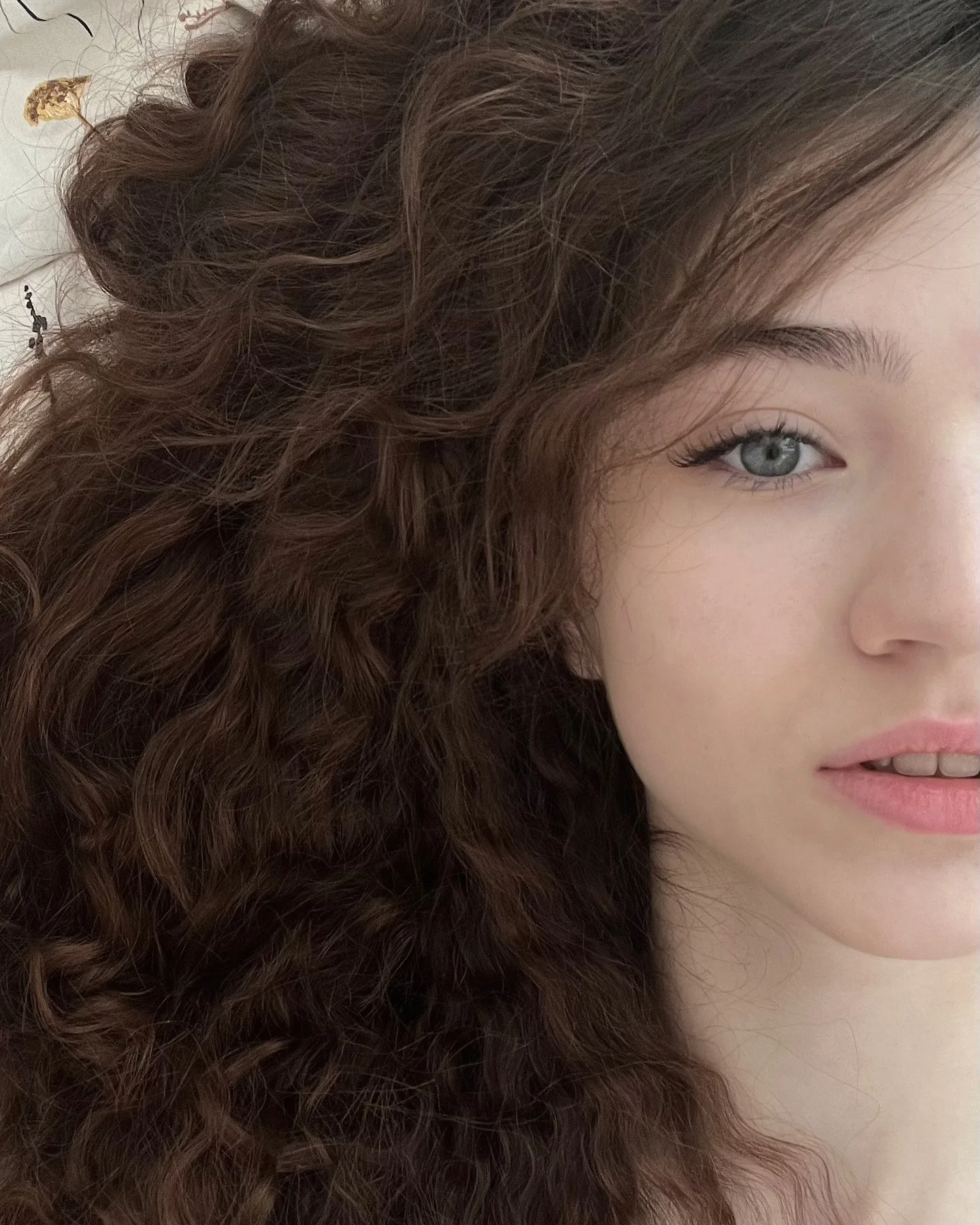 Close-up portrait of a woman with voluminous dark brown curly hair and blue eyes.