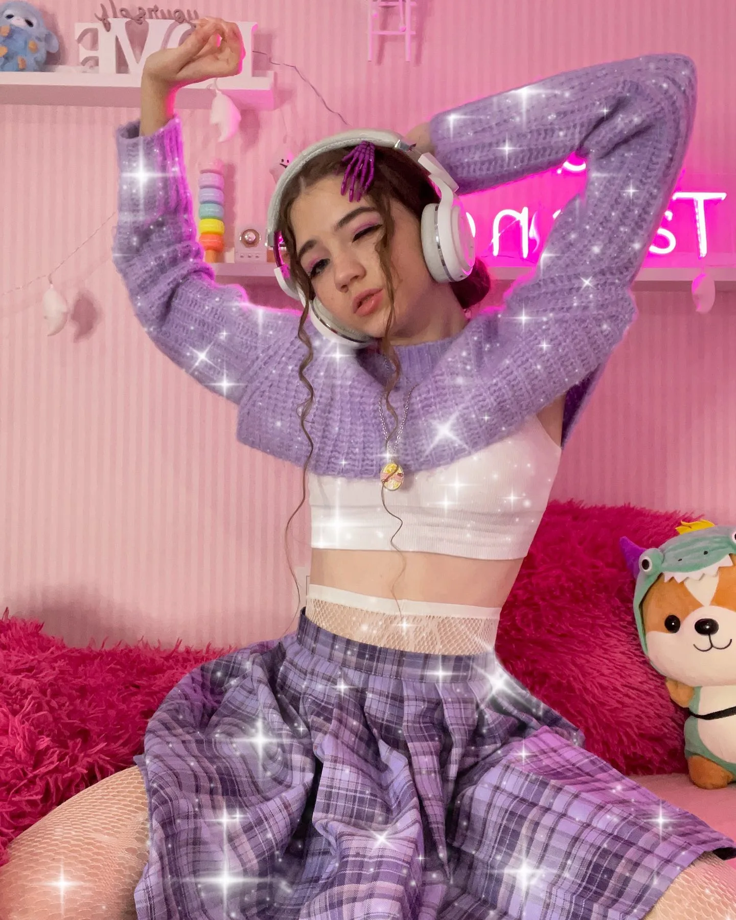 Dana poses in a purple plaid outfit with headphones in a pink room with sparkles.