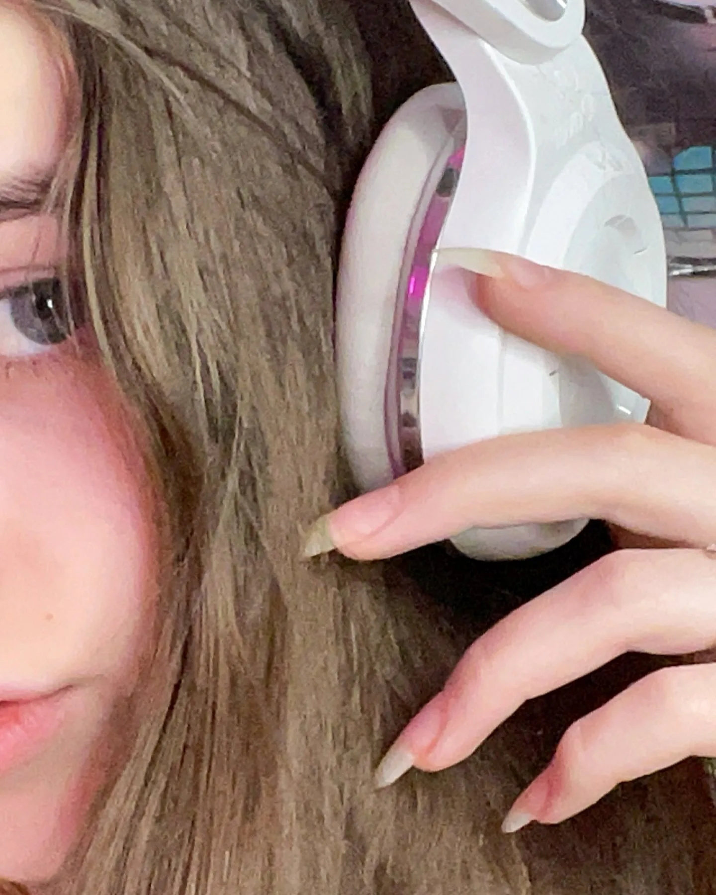 Close-up of a person with long brown hair wearing white headphones with pink LED lights, their hand resting on the ear cup.