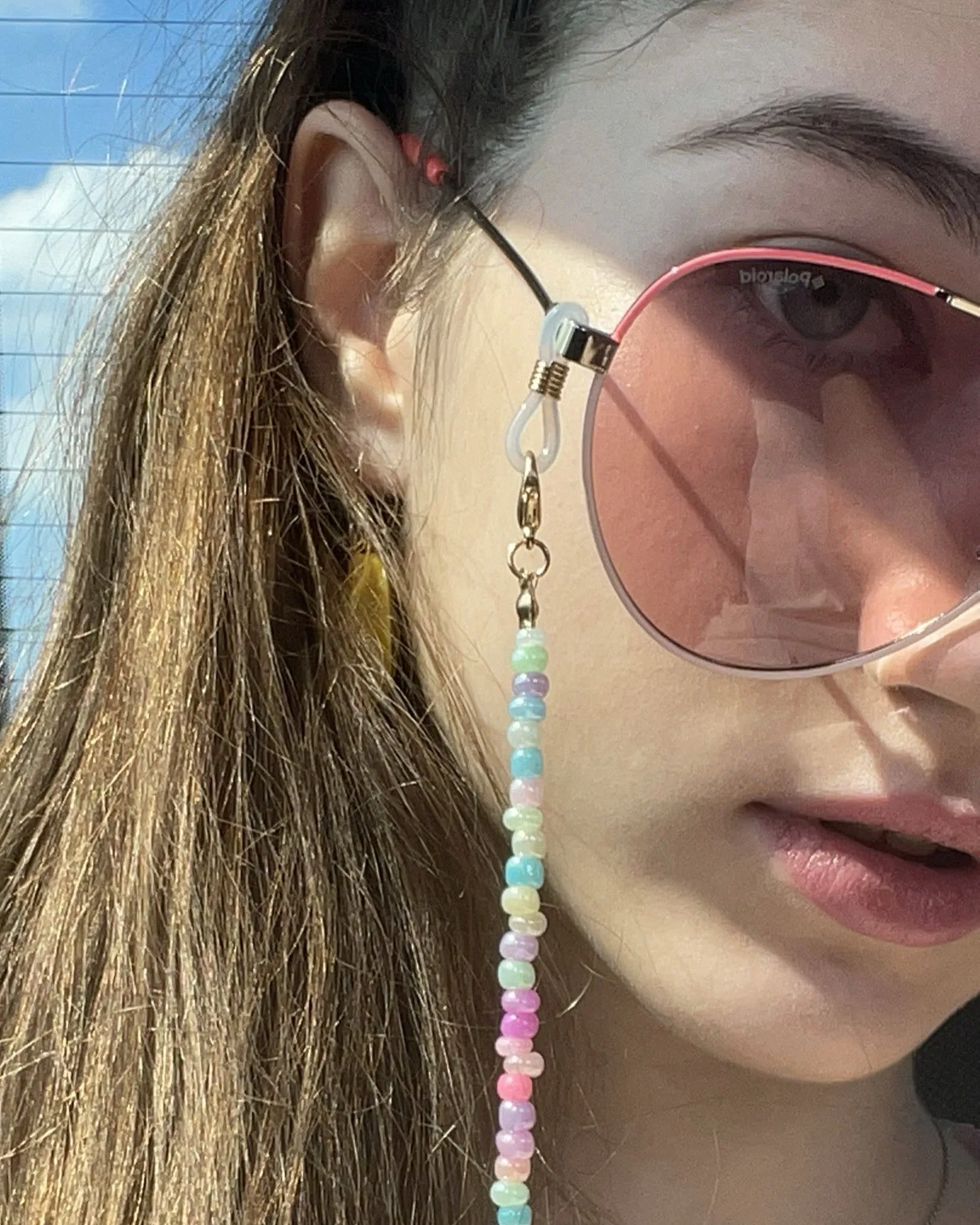 Close-up of a woman wearing pink-tinted sunglasses with a colorful beaded chain hanging from the frame.