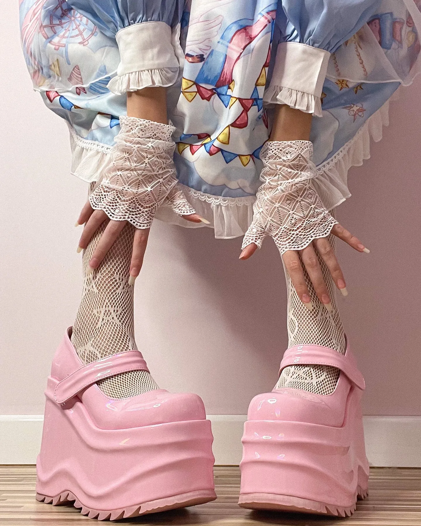 Close-up of pink platform shoes with fishnet socks and lace gloves, worn with a pastel blue dress featuring bunting patterns.