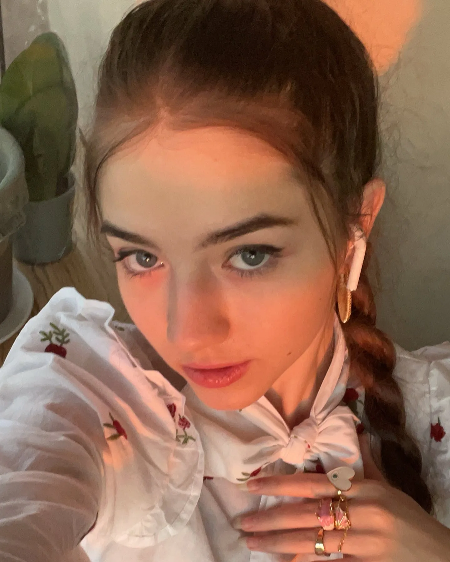 Close-up portrait of Dana with braided hair and white earbuds wearing a white blouse with red embroidery.