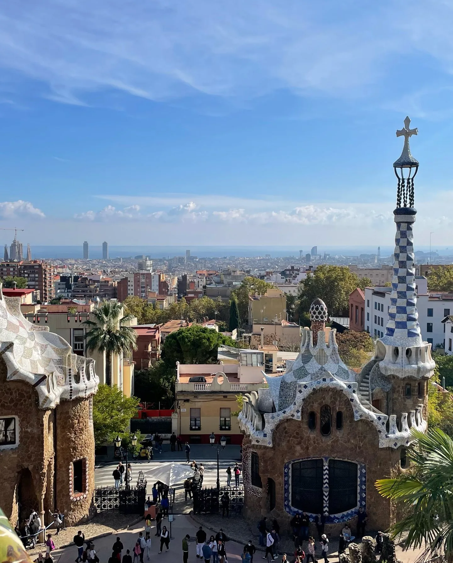 Panoramic view of Park Güell in Barcelona featuring Gaudí's mosaic-tiled architecture and the city skyline under a blue sky.