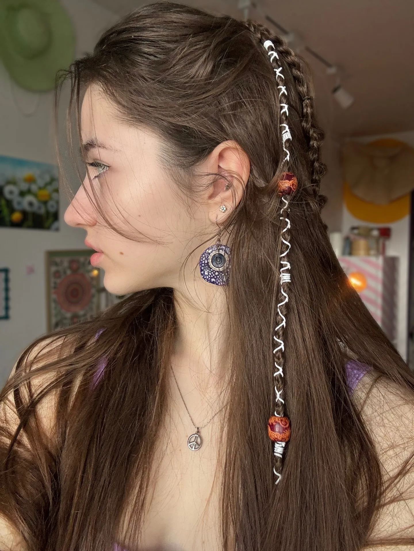Profile of Dana featuring a side braid adorned with colorful beads and silver rings, showcasing a bohemian hairstyle with large blue earrings.