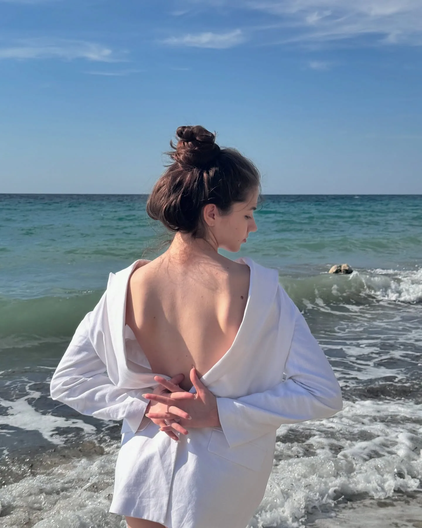 Woman in white shirt standing on beach looking at ocean